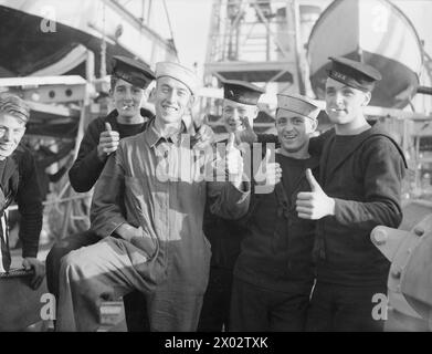 ANKUNFT DER ERSTEN FLOTTE AMERIKANISCHER ZERSTÖRER FÜR DIE ROYAL NAVY. 28. SEPTEMBER 1940, ROYAL DOCKYARD, DEVONPORT. DIE FLOTTE, DIE VON DER US-REGIERUNG IM RAHMEN DES ABKOMMENS ÜBERGEBEN WURDE, WAR VOLLSTÄNDIG VON BRITISCHEN BESATZUNGEN BESETZT. - "Daumen hoch" von Mitgliedern der britischen Marinecrew, die die Zerstörer in dieses Land gebracht haben. Zwei der Besatzungsmitglieder brachten amerikanische Marinekappen mit, die sie von der amerikanischen Besatzung des Zerstörers erhielten, die vor der Übergabe an Bord war Stockfoto