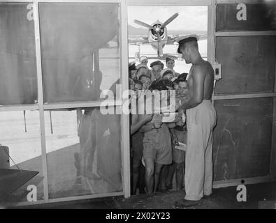 ZEITUNG DER BRITISCHEN PAZIFIKFLOTTE. AUGUST 1945, SYDNEY, AUSTRALIEN. PRODUKTION UND VERTRIEB DER EIGENEN ZEITUNG "PACIFIC POST" DER BRITISCHEN PAZIFIKFLOTTE DURCH DIE NAVY FÜR DIE NAVY. - Petty Officer Derrick W Condom von Nottingham, der Kopien der Pacific Post an einer Royal Naval Air Station im Pazifik verteilt Stockfoto