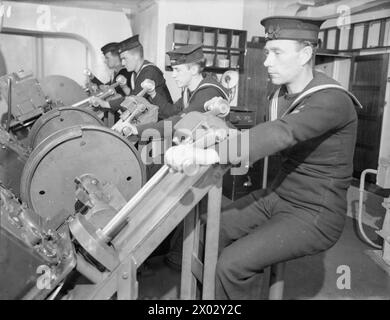 ENTWÄSSERUNG DES ROYAL NAVY-ZUGES AUF DEM MODERNEN SCHULSCHIFF. SEPTEMBER 1941 AN BORD DES ZERSTÖRER-DEPOT-SCHIFFES HMS TYNE. DIE DESTROYERMEN SIND AUSGEBILDET IN GESCHÜTZE, TORPEDOFEUER, U-BOOT-ABWEHR, SEEMANNSCHAFT UND SIGNALGEBUNG. ES WERDEN SCHIFFSMODELLE VERWENDET UND DIE BELEUCHTUNG IST SO ANGEORDNET, DASS SIE DIE EFFEKTE VON SCHEINWERFERN, STERNMUSCHELN UND GESCHÜTZBLITZEN ERZEUGT. - Männer trainieren als Waffenschichten und Trainer, die lernen, dem Waffendirektor zu folgen Stockfoto