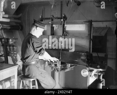 ENTWÄSSERUNG DES ROYAL NAVY-ZUGES AUF DEM MODERNEN SCHULSCHIFF. SEPTEMBER 1941 AN BORD DES ZERSTÖRER-DEPOT-SCHIFFES HMS TYNE. DIE DESTROYERMEN SIND AUSGEBILDET IN GESCHÜTZE, TORPEDOFEUER, U-BOOT-ABWEHR, SEEMANNSCHAFT UND SIGNALGEBUNG. ES WERDEN SCHIFFSMODELLE VERWENDET UND DIE BELEUCHTUNG IST SO ANGEORDNET, DASS SIE DIE EFFEKTE VON SCHEINWERFERN, STERNMUSCHELN UND GESCHÜTZBLITZEN ERZEUGT. - Hinter den Kulissen. Eine rückwärtige Schießerei manipuliert die Tasten, die beim Drücken die Spritzer steigen lassen Stockfoto