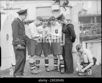 DIE ROYAL NAVY WÄHREND DES ZWEITEN WELTKRIEGS - vier Mitglieder des Fußballteams HMT MAN O'WAR tragen ihre Ausrüstung, während sie sich auf ihre nächste Eroberung an Bord des Schiffs Liverpool vorbereiten. Zwei weitere Crew-Mitglieder sind bei den Männern. Die Fußballmannschaft, die aus Mitgliedern der Crew des Trawlers besteht, hält den Rekord ihrer Basis, 20 ausgespielte Spiele, 19 gewonnene Spiele und eines ausgelost. Trotz der Unannehmlichkeiten, die das Leben an Bord des kleinen Schiffes auf See hat, nehmen sich die Besatzung im Hafen gegen andere Teams anderer Schiffe auf und gewinnen – dies ist ihre Idee, die Royal Navy, MAN O'WAR (HMT) zu ruhen. Stockfoto