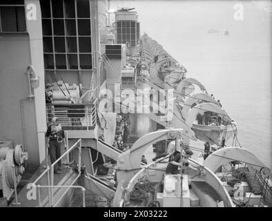 DIE KÖNIGIN MARY IM KRIEGSDIENST. 28. SEPTEMBER 1944, GREENOCK. DIE 84000 TONNEN SCHWERE CUNARD-LINER QUEEN MARY IN IHRER GRAUEN WEISSEN KRIEGSFARBE, ALS SIE SICH AUF EINE WEITERE ATLANTIKÜBERQUERUNG VORBEREITETE, DIE VERWUNDETE US-TRUPPEN NACH AMERIKA ZURÜCKBRACHTE. - Ich schaue auf dem Bootsdeck der KÖNIGIN MARY während der Rettungsbootübung im Hafen entlang Stockfoto