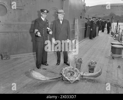 HMAS AUSTRALIA IN PLYMOUTH AN REFIT. AM 1. JULI 1945 TRAF PLYMOUTH, HMAS AUSTRALIA, EIN HOCHRANGIGES SCHIFF DER AUSTRALISCHEN MARINE, DAS VOR LEYTE VON EINEM JAPANISCHEN SELBSTMORDATTENTÄTER SCHWER BESCHÄDIGT WURDE, IN PLYMOUTH EIN, UM DORT UMZUBAUEN. DIE RT HON S M BRUCE, HOHER KOMMISSAR FÜR AUSTRALIEN, BEGLEITET VON ADMIRAL SIR RALPH LEATHAM, C IN C PLYMOUTH, BEGRÜSSTE DEN KOMMANDANTEN DES SCHIFFES, CAPTAIN J M ARMSTRONG, DSO, RAN UND DIE CREW BEI DER ANKUNFT. - Captain J M Armstrong zeigt dem Hochkommissar für Australien Teile des japanischen Selbstmordflugzeugs, das in der Schlacht von Leyte die Brücke des Schiffes getroffen hat Stockfoto