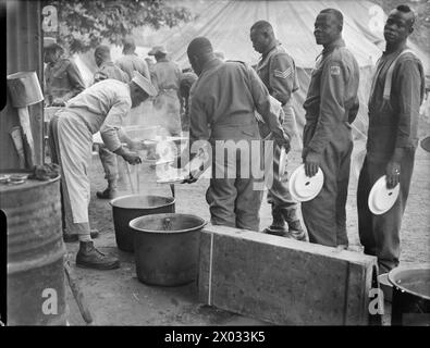 VICTORY MARCHERS CAMP IN LONDON: UNTERKUNFT IN KENSINGTON GARDENS, LONDON, ENGLAND, Großbritannien, 1946 - Männer verschiedener afrikanischer Regimenter stellen sich in ihrem Zeltlager in Kensington Gardens, London, für ihre Mittagsmahlzeit an Stockfoto