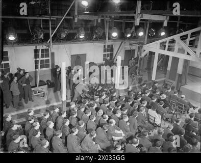 COASTAL COMMAND: PRODUKTION EINES FILMS DES MINISTERIUMS FÜR INFORMATION IN DEN PINEWOOD STUDIOS, IVER HEATH, BUCKINGHAMSHIRE, ENGLAND, VEREINIGTES KÖNIGREICH, MÄRZ 1942: Eine Filmszene von Coastal Command, einem Film der Crown Film Unit in den New Studios, Pinewood, in Iver Heath in Buckinghamshire. In dieser Szene wartet ein Publikum auf den Beginn einer RAF „Gang Show“ in einem hebridischen Dorfsaal. Der Rand des Geräts ist deutlich sichtbar, ebenso die Beleuchtungsbrücke oben im Bild. Im linken Hintergrund sind die Mitglieder der Produktionsteams zu sehen, im mittleren Hintergrund die Kamerabediener Stockfoto