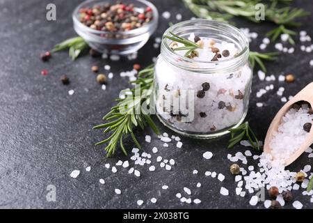 Salz mit frischem Rosmarin und Pfeffer auf dunkelgrauem, strukturiertem Tisch Stockfoto