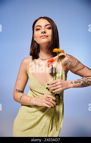 Eine junge Frau mit brünetten Haaren in einem gelben Kleid, die Blumen in einem ruhigen Studio hält. Stockfoto