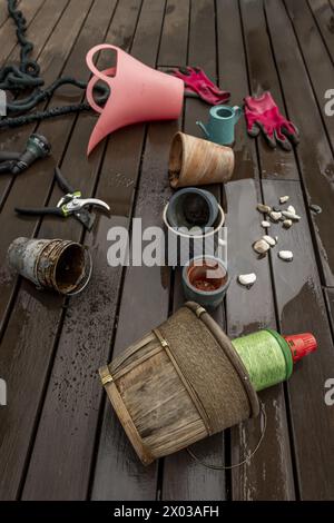 Düngung von Innenpflanzen mit Gartenwerkzeugen, Schutzhandschuhen, Flüssigdünger auf einer Terrasse mit nassen Holzböden Stockfoto