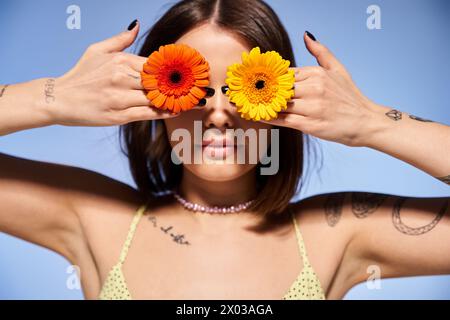 Eine junge Frau mit brünetten Haaren, die zwei Blumen vor den Augen hält, in einem Studio. Stockfoto