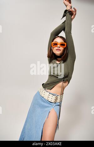 Eine schicke Brünette posiert in einem stilvollen Rock und einer Sonnenbrille und strahlt Selbstvertrauen und Eleganz in einem Studio-Ambiente aus. Stockfoto