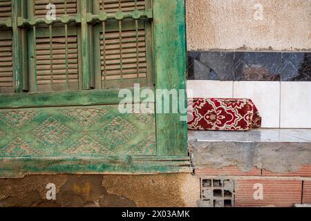 Detail einer Mashrabiya oder traditionellen geschnitzten Holzleinwand neben einer gekachelten Bank mit rotem Kissen an der Außenseite eines arabischen Hauses im Stockfoto