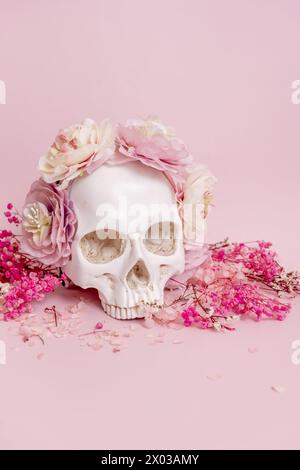 Weißer Schädel sieht hübsch aus, umgeben von getrockneten Blumen und Pflanzen mit Zweigen auf einer weichen rosa Oberfläche Stockfoto