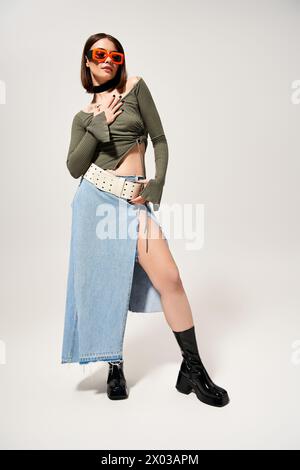 Eine stilvolle brünette Frau posiert in einem Rock und Stiefeln im Studio. Stockfoto