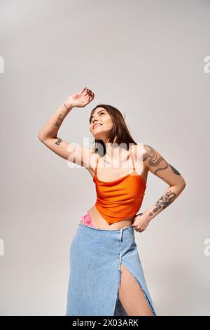 Eine junge Frau mit brünetten Haaren, die ein orangefarbenes Oberteil und einen blauen Rock trägt, wirbelt in einer lebendigen Studioatmosphäre. Stockfoto