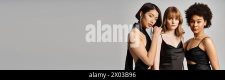 Drei schöne Frauen verschiedener ethnischer Gruppen aus Kaukasiern, Asiaten und Afroamerikanern stehen elegant zusammen vor grauem Atelierhintergrund. Stockfoto