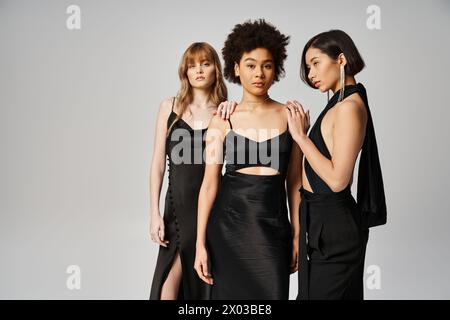Eine Gruppe eleganter Frauen mit unterschiedlichem kulturellen Hintergrund, die nebeneinander in einem Studio mit grauem Hintergrund stehen. Stockfoto