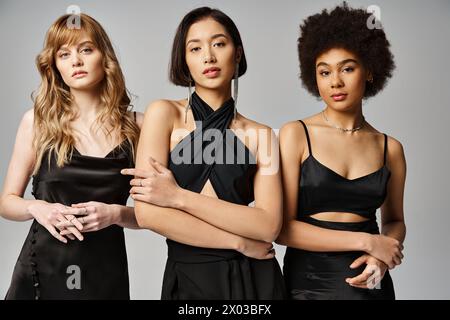 Eine vielfältige Gruppe von drei Frauen, kaukasische, asiatische und afroamerikanische, die zusammen auf grauem Atelierhintergrund stehen. Stockfoto