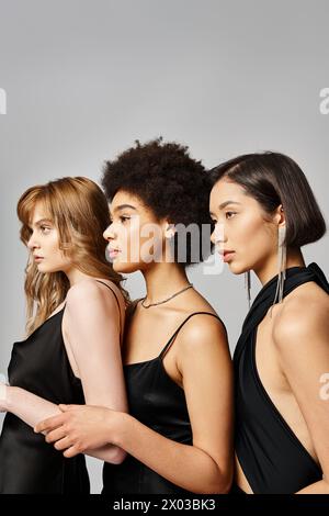 Eine vielfältige Gruppe eleganter Frauen unterschiedlicher Ethnien, die in Harmonie vor grauem Atelierhintergrund stehen. Stockfoto