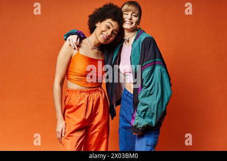 Zwei schöne Frauen mit unterschiedlichem kulturellen Hintergrund stehen zusammen in einem Atelier vor einem orangen Hintergrund. Stockfoto