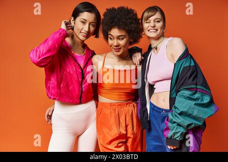 Drei Frauen verschiedener Ethnien stehen zusammen vor einem orangen Hintergrund und zeigen multikulturelle Schönheit und Einheit. Stockfoto