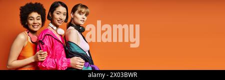 Eine Gruppe von Frauen unterschiedlicher Ethnien und Kulturen, die vor einem orangen Hintergrund nebeneinander stehen. Stockfoto