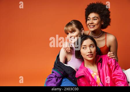 Zwei Frauen verschiedener Rassen posieren liebevoll mit einem glücklichen Kind vor einem orangen Studio-Hintergrund. Stockfoto