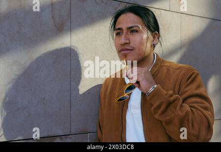 Junger ecuadorianischer Mann in einer stilvollen braunen Jacke mit Sonnenbrille, um die städtische Umgebung zu erkunden. Stockfoto
