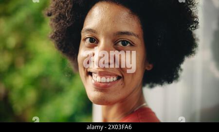 Nahaufnahme Porträt einer glücklichen jungen Latina mit braunen Augen, Afrohaar und Nase Piercing für die Kamera. Schöne vielfältige multiethnische Schwarze Hispanic weibliche lächelnd auf grünem Natur Hintergrund. Stockfoto
