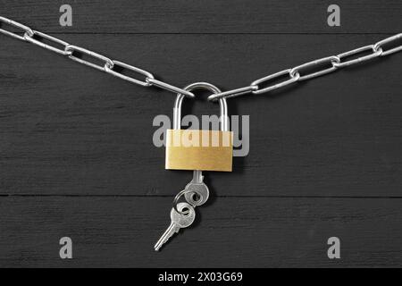 Vorhängeschloss aus Stahl mit Schlüsseln und Kette auf schwarzem Holztisch, Draufsicht Stockfoto