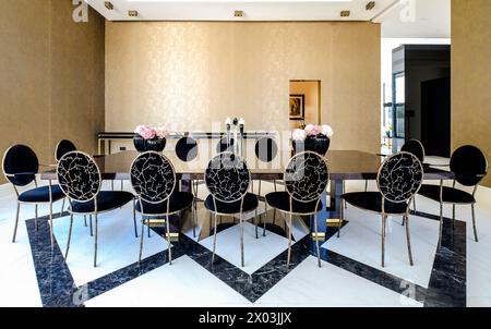 HAMALA, BAHRAIN - 2. MÄRZ 2019: Eleganter moderner Speisesaal mit reflektierendem Marmortisch und Glasvasen mit rosa Blumen in einer Luxusvilla. Stockfoto