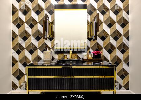 HAMALA, BAHRAIN - 2. MÄRZ 2019: Elegantes, modernistisches Waschbecken aus schwarzem Marmor mit Spiegel und Goldbeschlägen und einer gefliesten Wand im Badezimmer einer Luxusvilla. Stockfoto