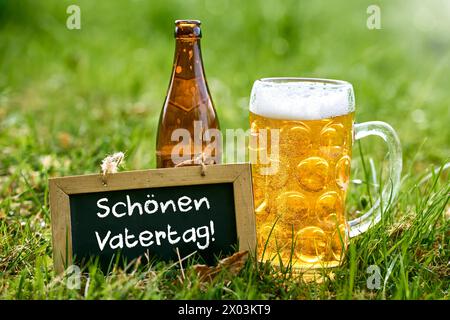 9. April 2024: Vatertaggrüße: Happy Vatertag auf einer Tafel auf einer Wiese mit einem Bierkrug und einer Bierflasche. FOTOMONTAGE *** Vatertagsgrüße: Schön Vatertag auf einer Tafel in einer Wiese mit einem Bierkrug und einer Bierflasche. FOTOMONTAGE Stockfoto