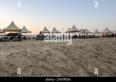 Liegestühle am Strand bei Sonnenuntergang in Meerwasser, Binnenmeer, ein Top-Touristenziel in Khor Al Adaid Beach Stockfoto