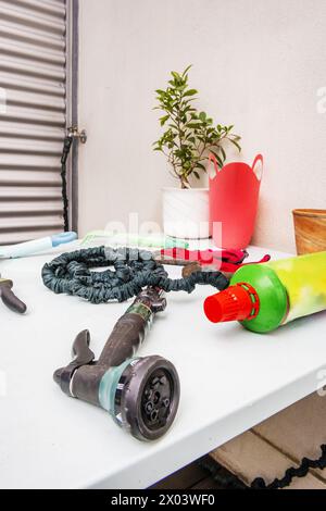 Ein hellblauer Tisch aus glattem Metall, gefüllt mit Gartenobjekten, neben einem Topf Ficus benjamina und einem Diffusorkopf aus einem Schlauch im Vordergrund Stockfoto