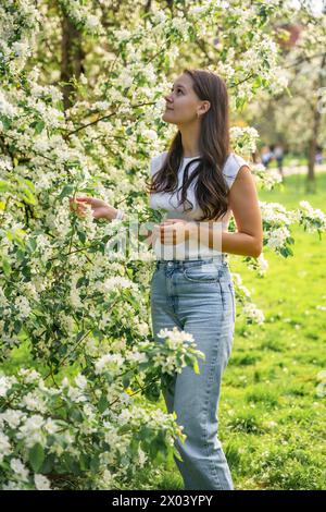 Junge Frau, die im Park in der Nähe eines Birnenbaums steht, der im Frühjahr in Prag mit weißen Blüten blüht Stockfoto