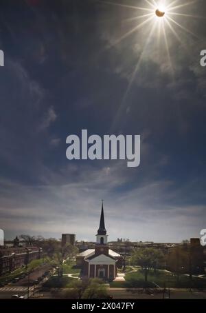 Blick auf die Stadt im Mittleren Westen im Frühling während teilweiser Sonnenfinsternis, wobei der Mond einen großen Teil der hellen Nachmittagssonne bedeckt; Straße und Gebäude im Vordergrund Stockfoto