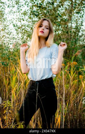 Schönes junges Mädchen, das ein leeres graues T-Shirt und eine schwarze Jeans trägt, posiert im frühen warmen Herbst vor hohem grünen und gelben Gras. Stockfoto