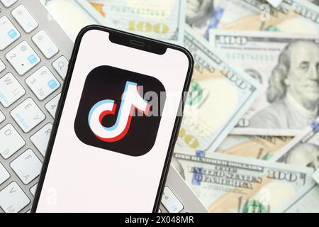 KIEW, UKRAINE - 1. APRIL 2024 TikTok- oder Douyin-Symbol auf dem Smartphone-Bildschirm auf vielen usd-Geldscheinen. IPhone-Display mit App-Logo und Dollarscheine mit weißer Tastatur Stockfoto