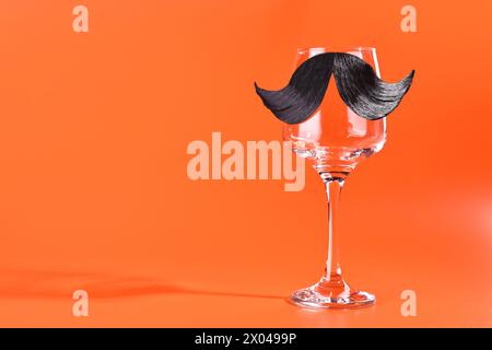 Männergesicht aus künstlichem Schnurrbart und Weinglas auf orangefarbenem Hintergrund. Leerzeichen für Text Stockfoto
