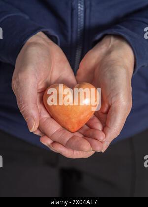 Eine ältere Frau hält eine Herzform in ihren Handflächen Stockfoto