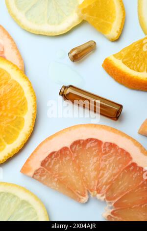 Gebrochene Hautpflegeampulle mit Vitamin C und Scheiben verschiedener Zitrusfrüchte auf hellblauem Hintergrund, Nahaufnahme Stockfoto