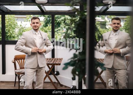 Der junge Bräutigam schließt den Knopf an seiner Jacke. Spiegelbild eines Mannes in einem Fenster Stockfoto