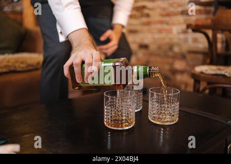 Der Prozess des Menschen, Whiskey in stilvolle Gläser zu gießen. Hintergrund der Ziegelmauer Stockfoto