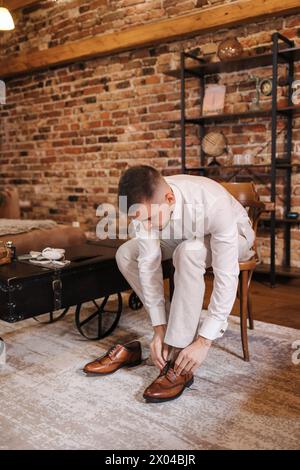 Ein gutaussehender Mann trägt braune Retro-Schuhe, während er auf dem Stuhl sitzt. Hintergrund der Ziegelmauer. Stockfoto