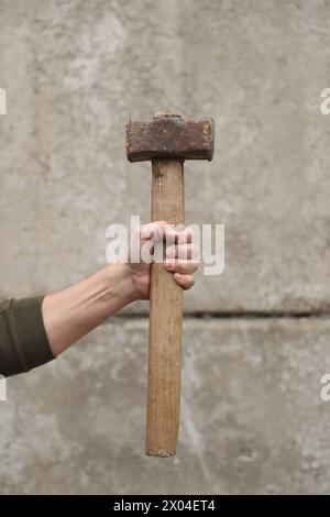 Mann mit Vorschlaghammer nahe der grauen Wand, Nahaufnahme Stockfoto