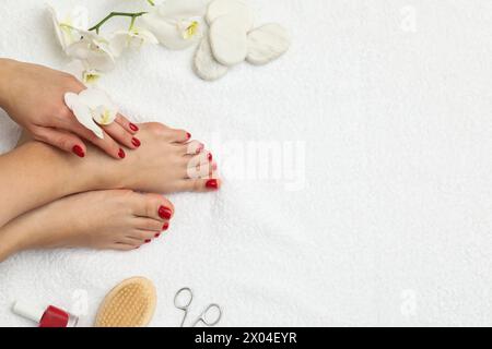 Frau mit stilvollen roten Zehennägeln nach Pediküre und Orchideenblüten auf weißem Frotteetuch, Blick von oben. Leerzeichen für Text Stockfoto