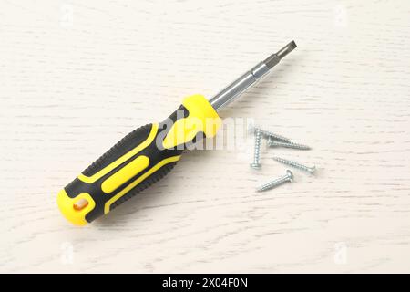 Schraubendreher mit gelbem Griff und Schrauben auf weißem Holztisch, flach gelegt Stockfoto