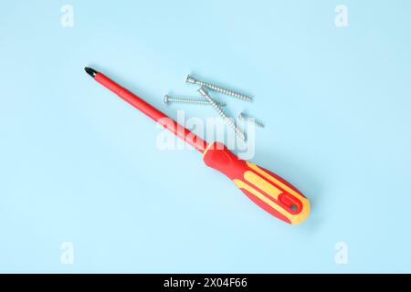Schraubendreher mit rotem Griff und Schrauben auf hellblauem Hintergrund, flach gelegt Stockfoto