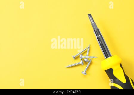 Schraubendreher mit schwarzem Griff und Schrauben auf hellgelbem Hintergrund, flach gelegt. Leerzeichen für Text Stockfoto