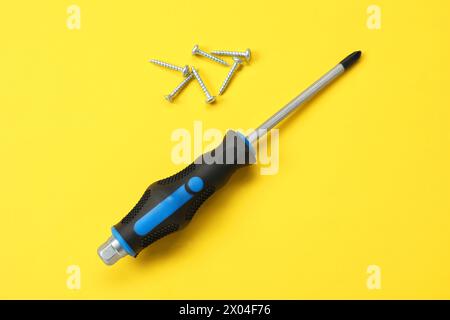 Schraubendreher mit schwarzem Griff und Schrauben auf gelbem Hintergrund, flach gelegt Stockfoto